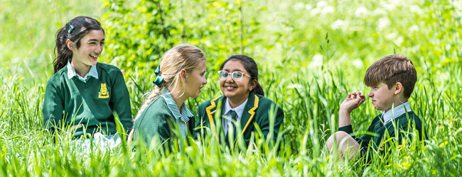 Gespräch in der Wiese von Schülern einer High School in Großbritannien Vier Schüler sitzen im Gras mit Uniformen einer High School in England